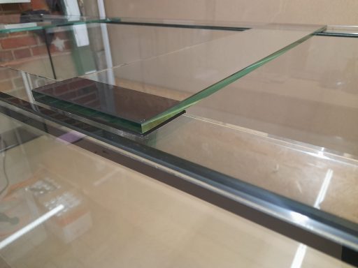 Ein großes, leeres Aquarium mit einem weißen Untergestell steht in einem hellen Raum.