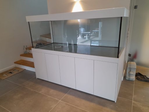 Ein großes, leeres Aquarium mit einem weißen Untergestell steht in einem hellen Raum.