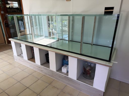 Ein großes, leeres Aquarium auf einem weißen Unterschrank steht in einem Raum.